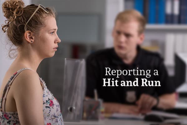 A woman looking shocked and worried, sitting on the other side of a desk from a man who is helping her file a report, with the words reporting a hit and run