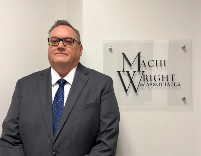 Daniel Wright, lead attorney, beside the Machi Wright & Associates office sign